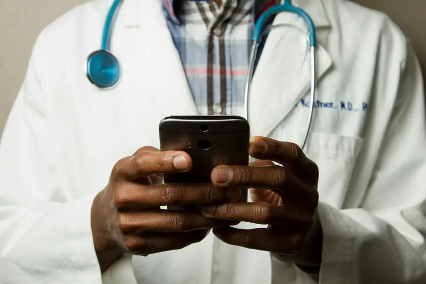 Médico de jaleco e estetoscópio consultando o celular